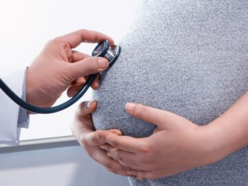 Image of a Doctor's hand holding a stethoscope on a pregnant women's stomach